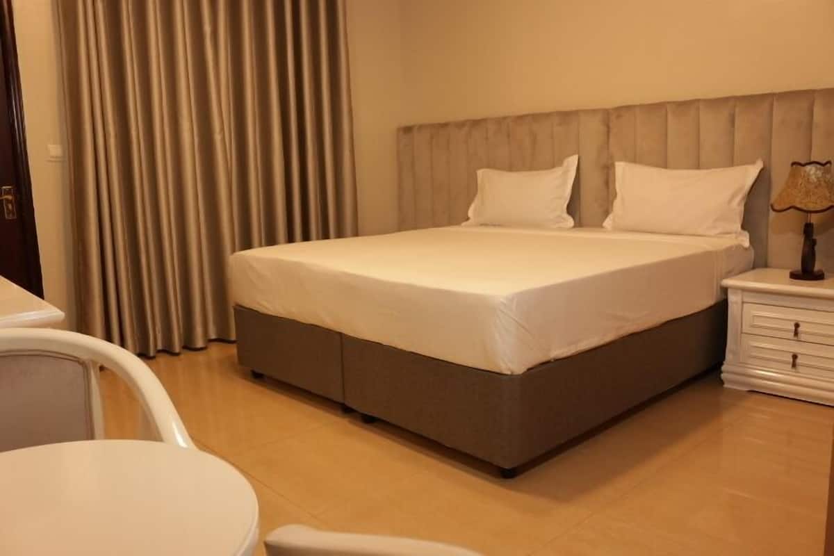 A hotel room with a bed, a bedside table, a chair, and a curtain.