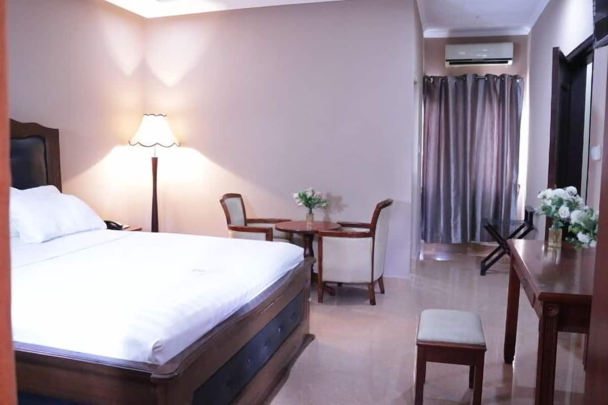 A hotel room with a bed, a desk, a chair, a small table, and a window with curtains.