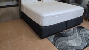 Ein modernes Schlafzimmer mit einem großen Bett, einem Kopfteil mit vertikalen Paneelen, einem grauen Sessel und einem Teppich mit Muster.