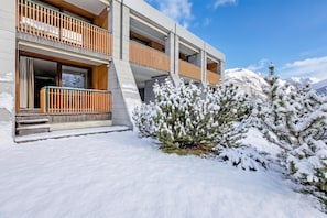 Un bâtiment moderne à plusieurs étages, doté d’un balcon, avec un paysage enneigé et des montagnes en arrière-plan.