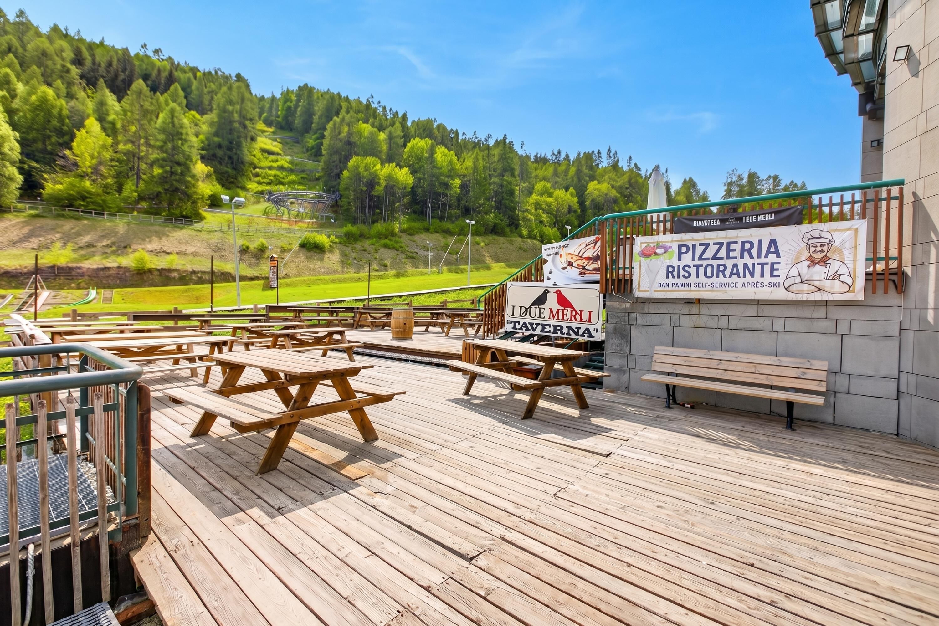 A wooden deck with picnic tables and benches, a sign for a pizzeria and tavern, and a view of a forested hillside.