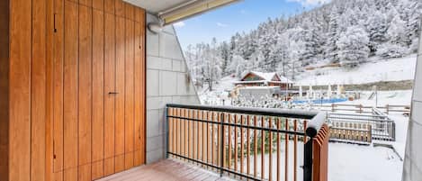 A wooden balcony with a metal railing overlooking a snowy landscape with buildings.