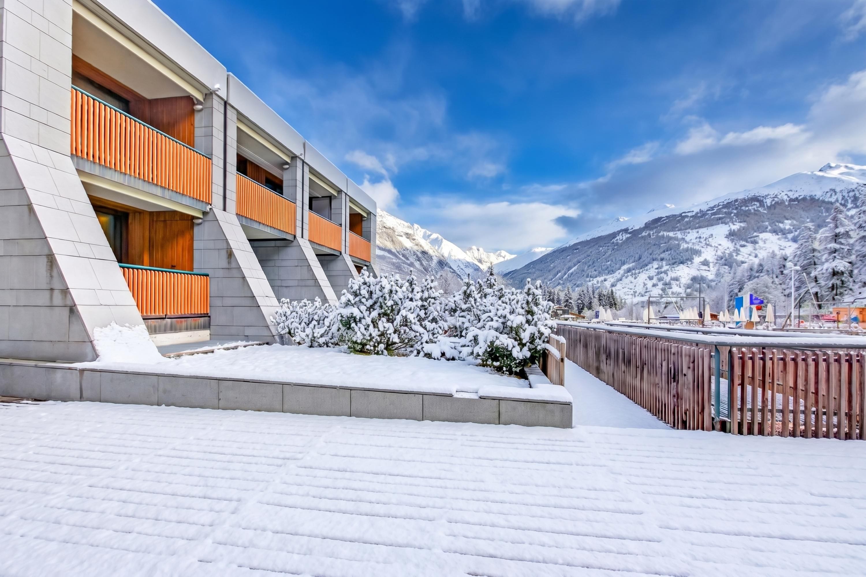 A modern building with a snow-covered landscape and mountains in the background.