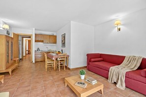 En stue med en rød sofa, et sofabord med en plante, et spiseområde med bord og stole, og et køkken i baggrunden.