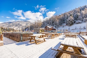 A wooden deck with picnic tables and a building with a sloped roof. - Hercules's House Ski-in/ski-out (Bardonecchia)