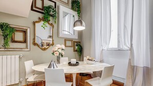 Ein Essbereich mit einem runden Tisch, weißen Stühlen, einer Blumenvase, einer Kerze und einer Lampe.
