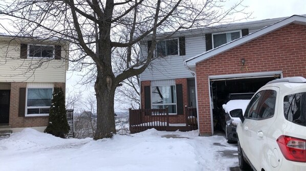 A residential area with a garage door open, a white car parked in front, and a snow-covered driveway.
