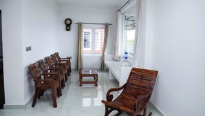 Un pasillo con sillas y mesa de madera, un reloj y una ventana con cortinas.
