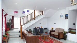 Amplia sala de estar con escalera de madera, sofá, mesa de centro y televisor. Hay plantas en macetas y un acuario.
