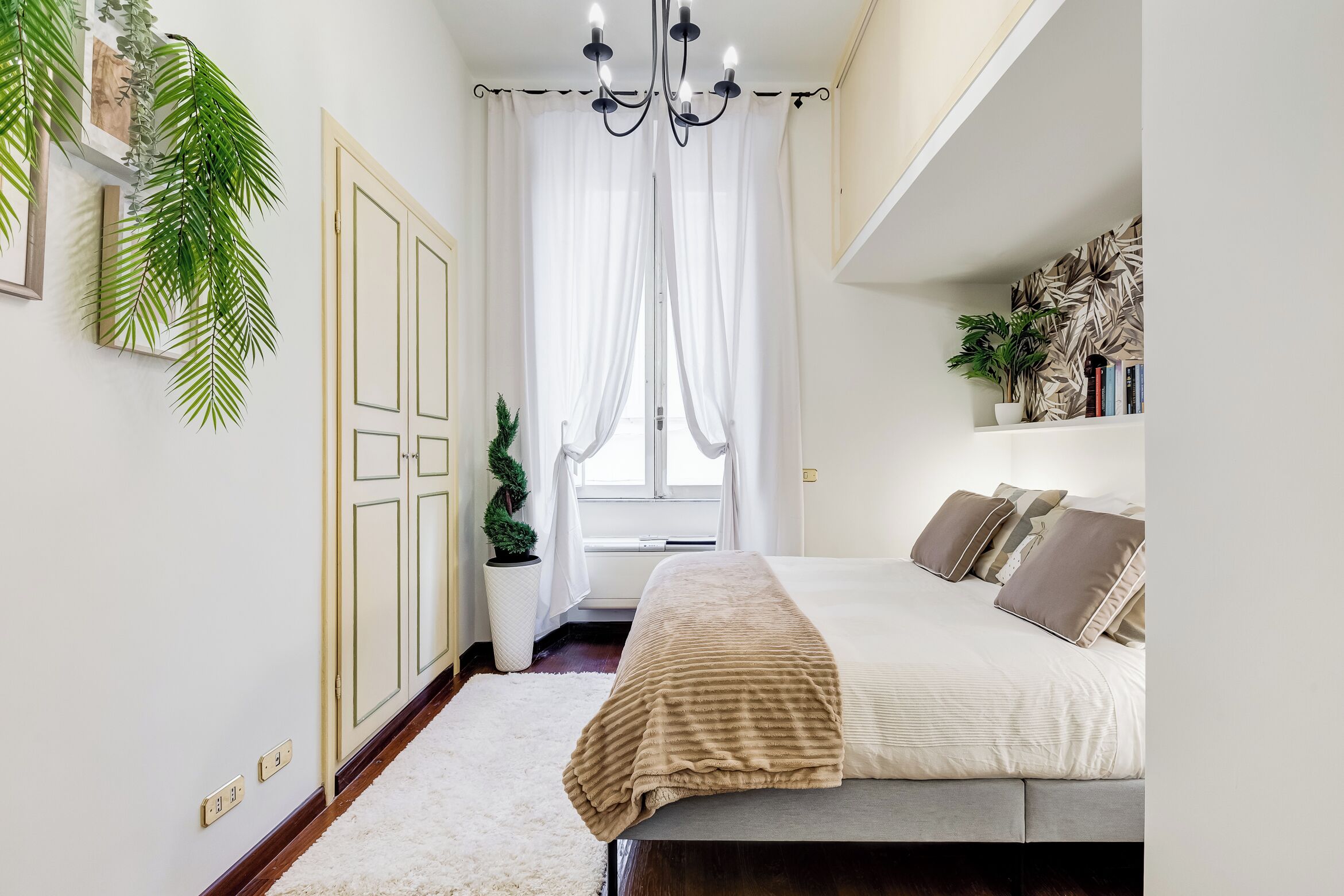 Ein Schlafzimmer mit einem Bett, einer Chandelier, einem Fenster mit Vorhängen und einer Zimmerpflanze.
