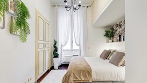 A bedroom with a bed, a chandelier, a window with curtains, and a potted plant. - PIAZZA DI SPAGNA FABULOUS AND COZY APARTMENT (Roma)