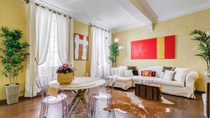 A living room with a round dining table, clear chairs, a white sofa, and a cowhide rug. There are two potted plants and a red and yellow painting on the wall. - PIAZZA DI SPAGNA FABULOUS AND COZY APARTMENT (Roma)