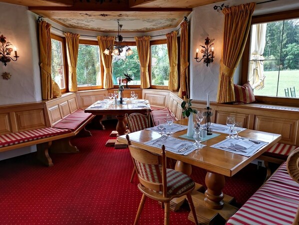 A dining area with a wooden table set for four, benches along the walls, and large windows with curtains. - Landhotel zur Grenze (Maierhöfen)