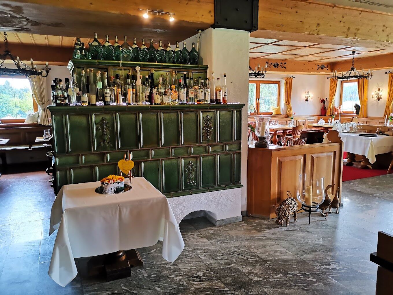 A restaurant with a bar area, a dining table with a cake, and a chandelier.
