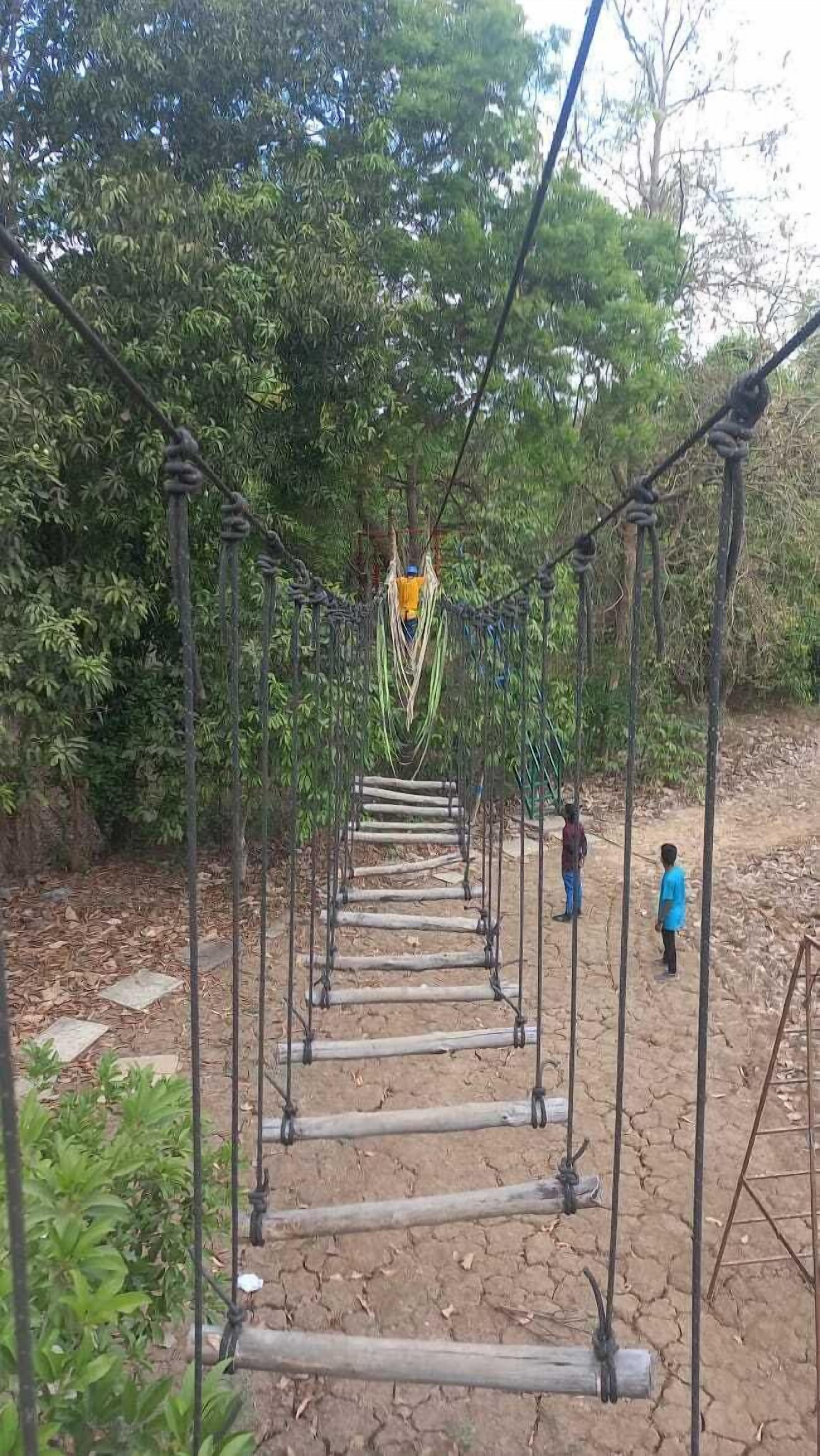 Un puente colgante en un área boscosa con dos personas caminando sobre él.