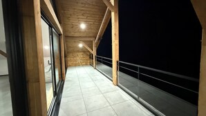 Ein Korridor mit Holzbalken und Fliesenboden, der zu einem Balkon mit Metallgeländer führt.