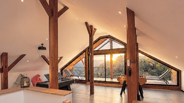 Ein großzügiges Loft mit hohen Decken, freiliegenden Holzbalken und großen Fenstern mit Blick ins Freie.