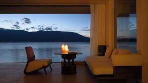 Habitación moderna con vistas al agua y a las montañas. Incluye un sofá, una silla y una mesa con velas.