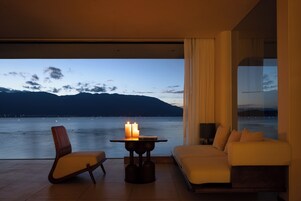 Habitación moderna con vistas al agua y a las montañas. Incluye un sofá, una silla y una mesa con velas.