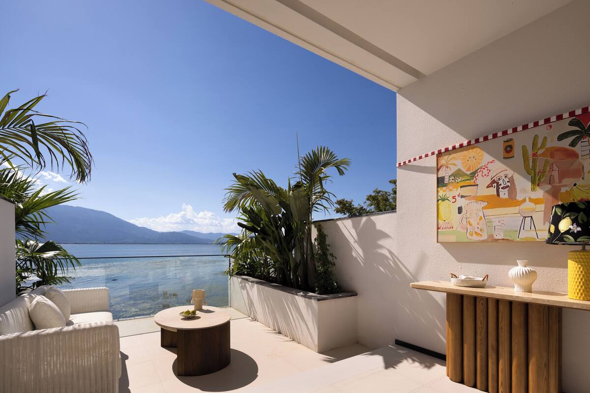 Ein Balkon mit Meerblick, eine Korbsitzgruppe, ein runder Tisch und eine Holztresen.