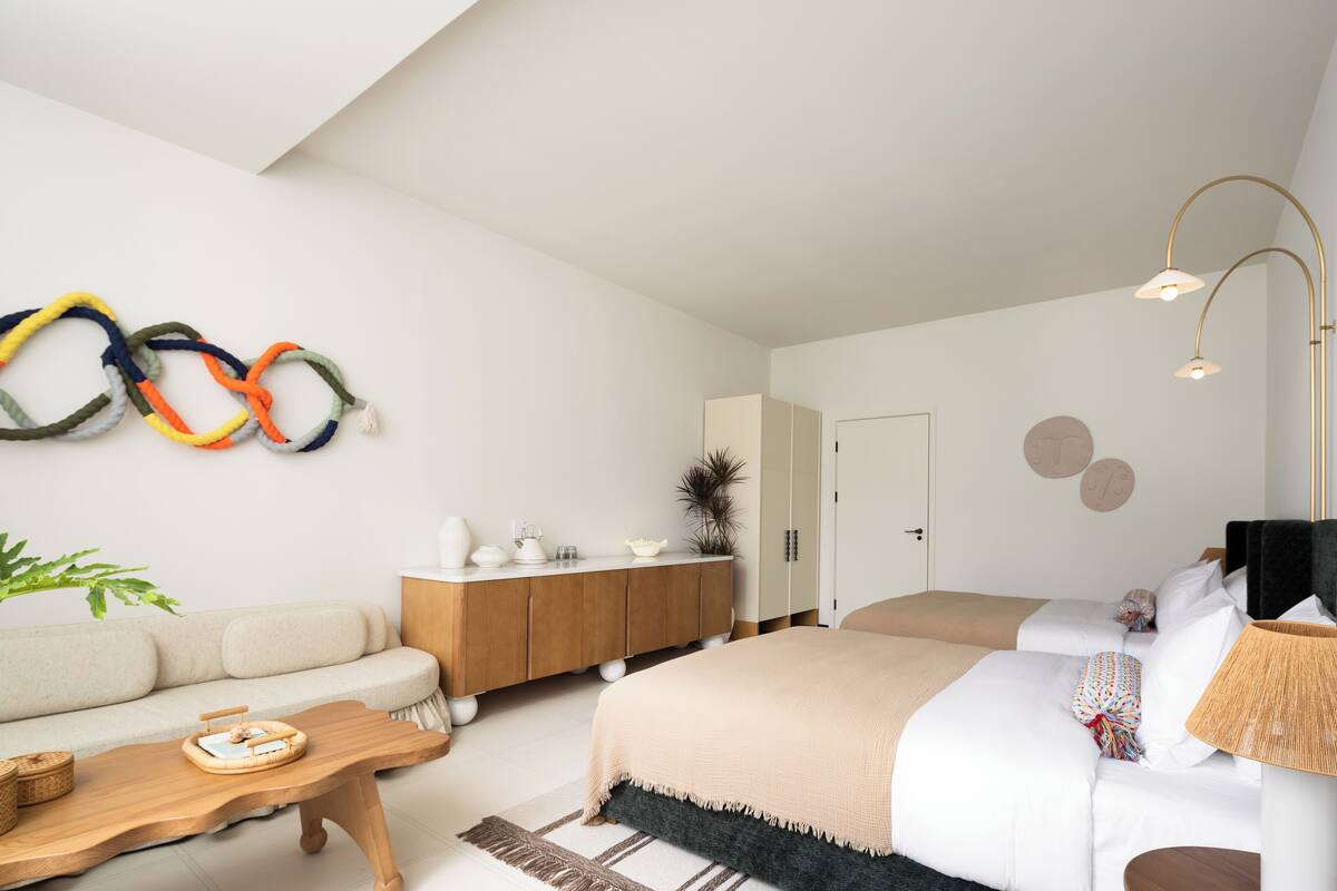 Ein modernes Schlafzimmer mit einer Couch, einem Holztischchen, einem Bett mit beiger Decke, einer Nachttischlampe und einer Wandlampe.