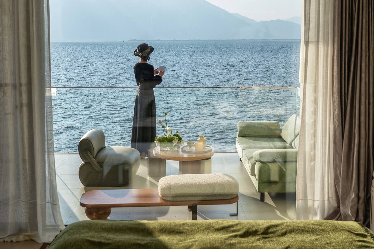 Ein Schlafzimmer mit einem großen Bett, einem Sofa und einem Couchtisch. Durch das Fenster ist Meer und Berge zu sehen.