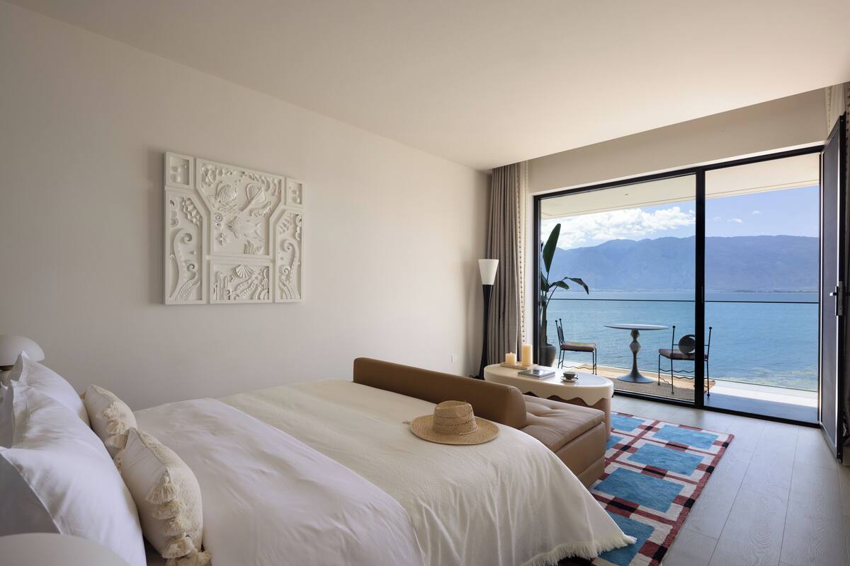 Ein Hotelzimmer mit Bett, einer Couch, einem kleinen Tisch mit Kerze und Meerblick durch ein großes Fenster.