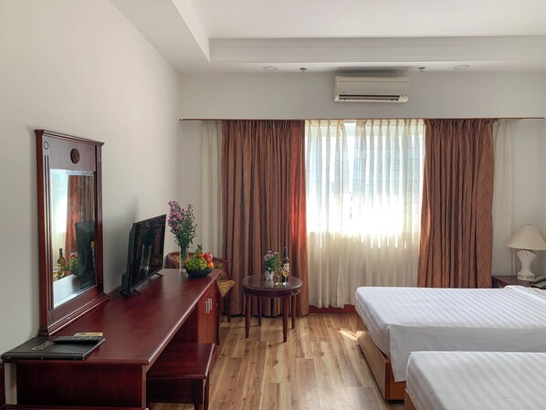 Habitación de hotel con escritorio de madera, cama, mesa redonda con un florero y un amplio ventanal con cortinas.