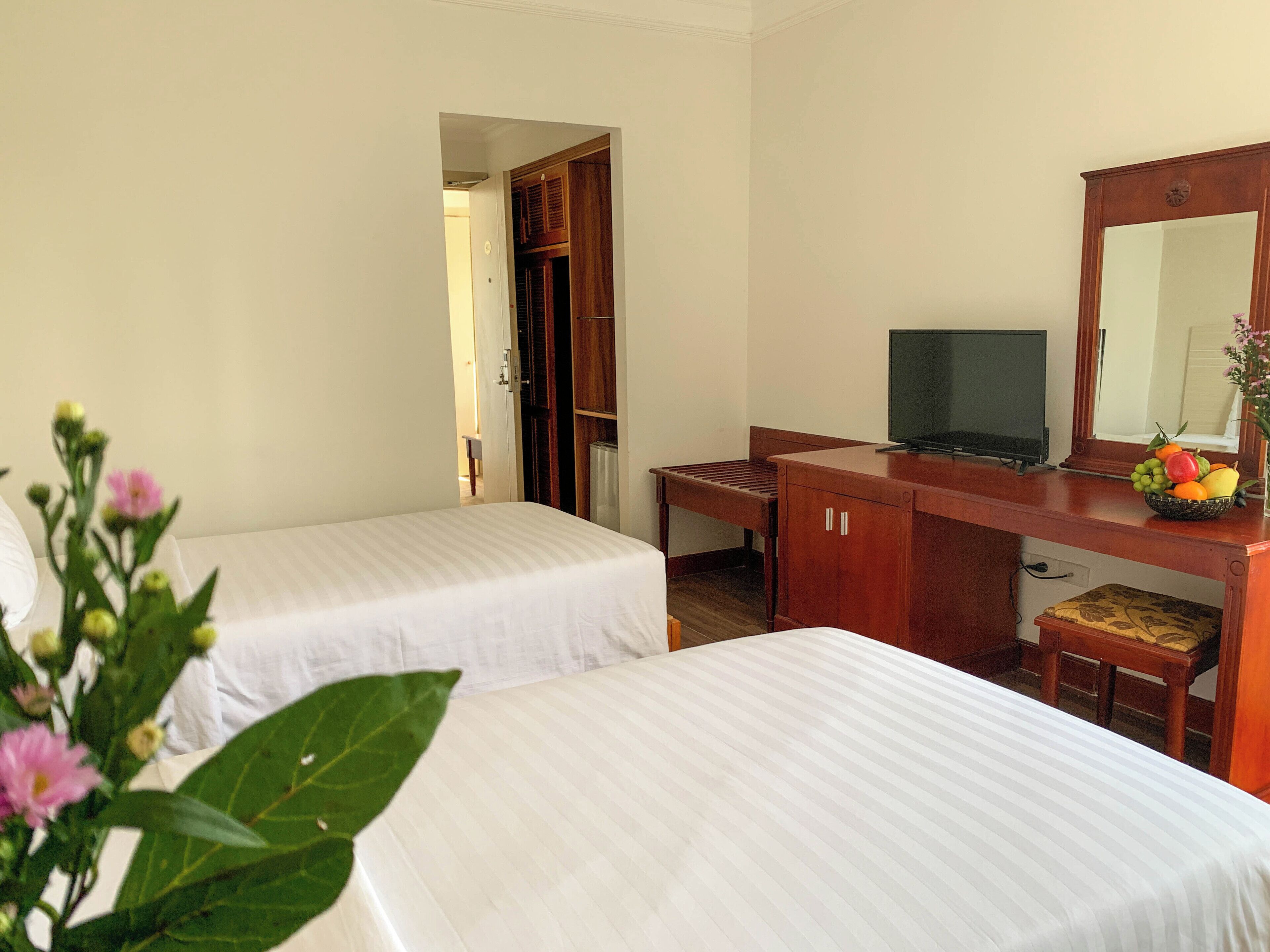 A hotel room with two beds, a desk with a computer, a small table, and a mirror.