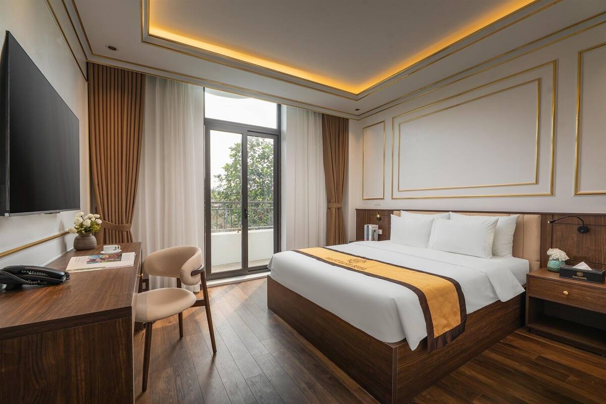 Una habitación de hotel con una cama grande, un escritorio con teléfono, una silla y una televisión.