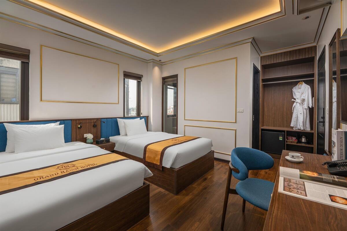 Una habitación de hotel con dos camas, un escritorio, una silla, un armario y un espejo.