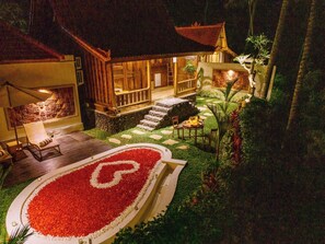 Un bâtiment traditionnel en bois, doté d’un toit de chaume, entouré d’un jardin bien entretenu, avec un chemin de pierre menant à une terrasse en bois.