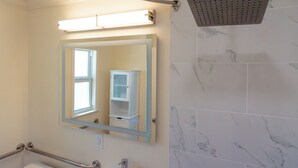 Une salle de bain équipée d’une douche, d’un miroir et d’une barre d’appui.