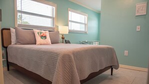 Une chambre à coucher avec un lit, deux fenêtres, une table de chevet et une lampe.
