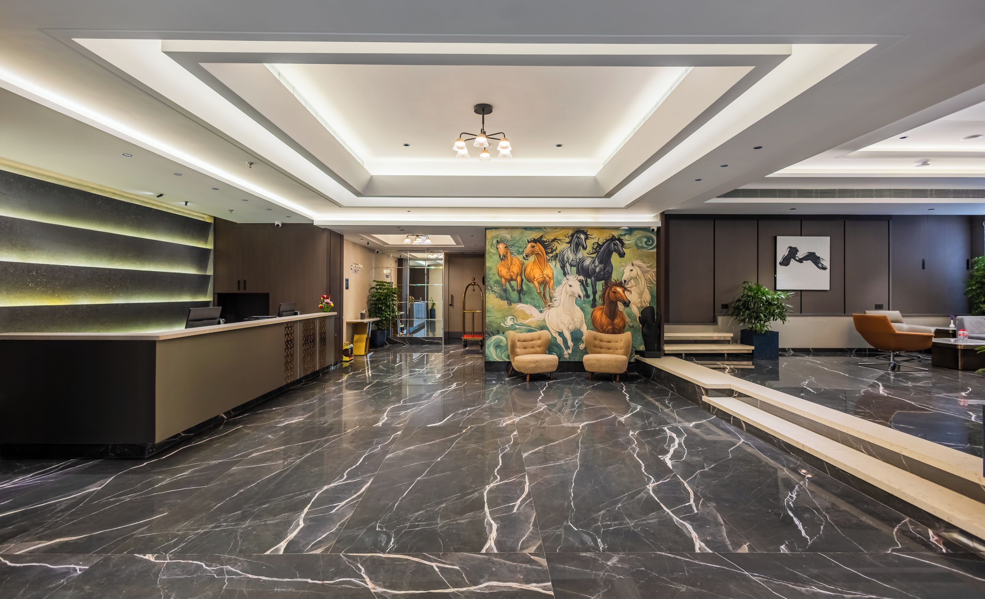 A modern hotel lobby with a reception desk, seating area, and a mural of horses.