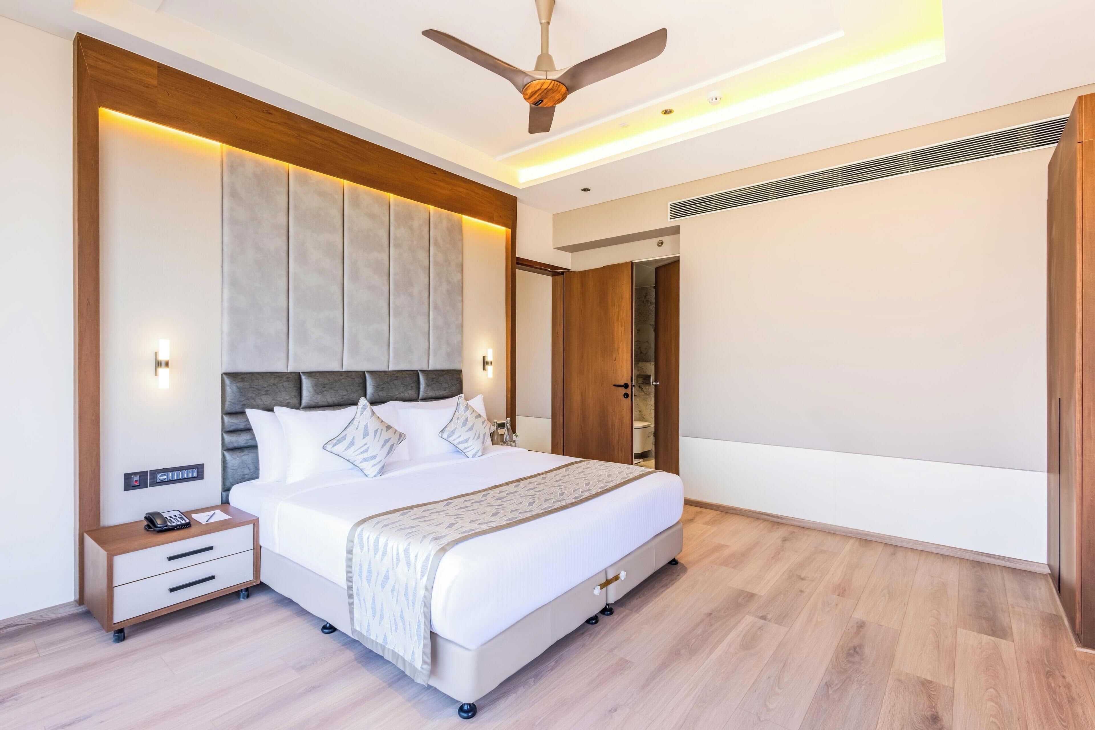 Una habitación de hotel moderna con una cama grande, una mesita de noche con teléfono y un ventilador de techo.