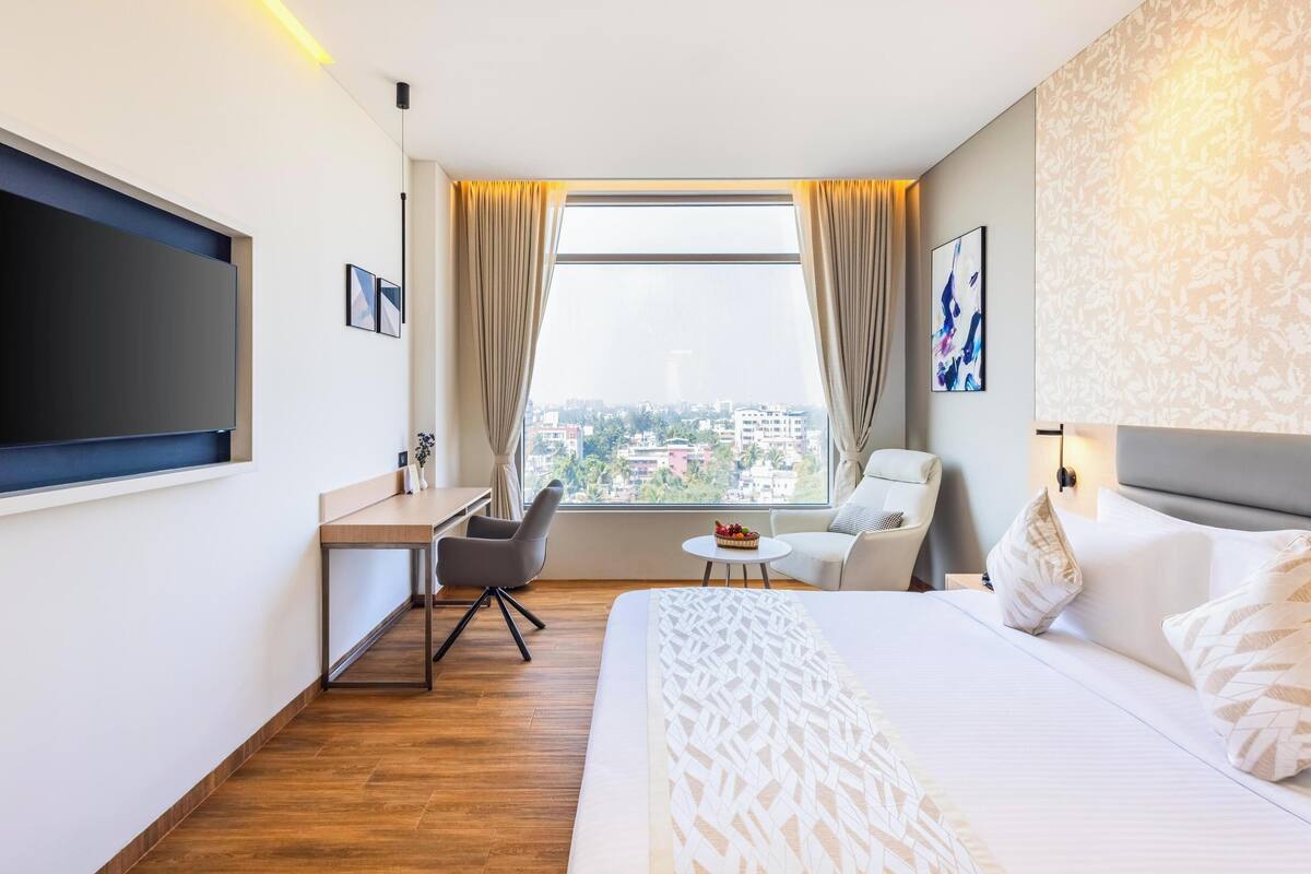 A hotel room with a bed, a desk, a chair, a TV, and a window with curtains.