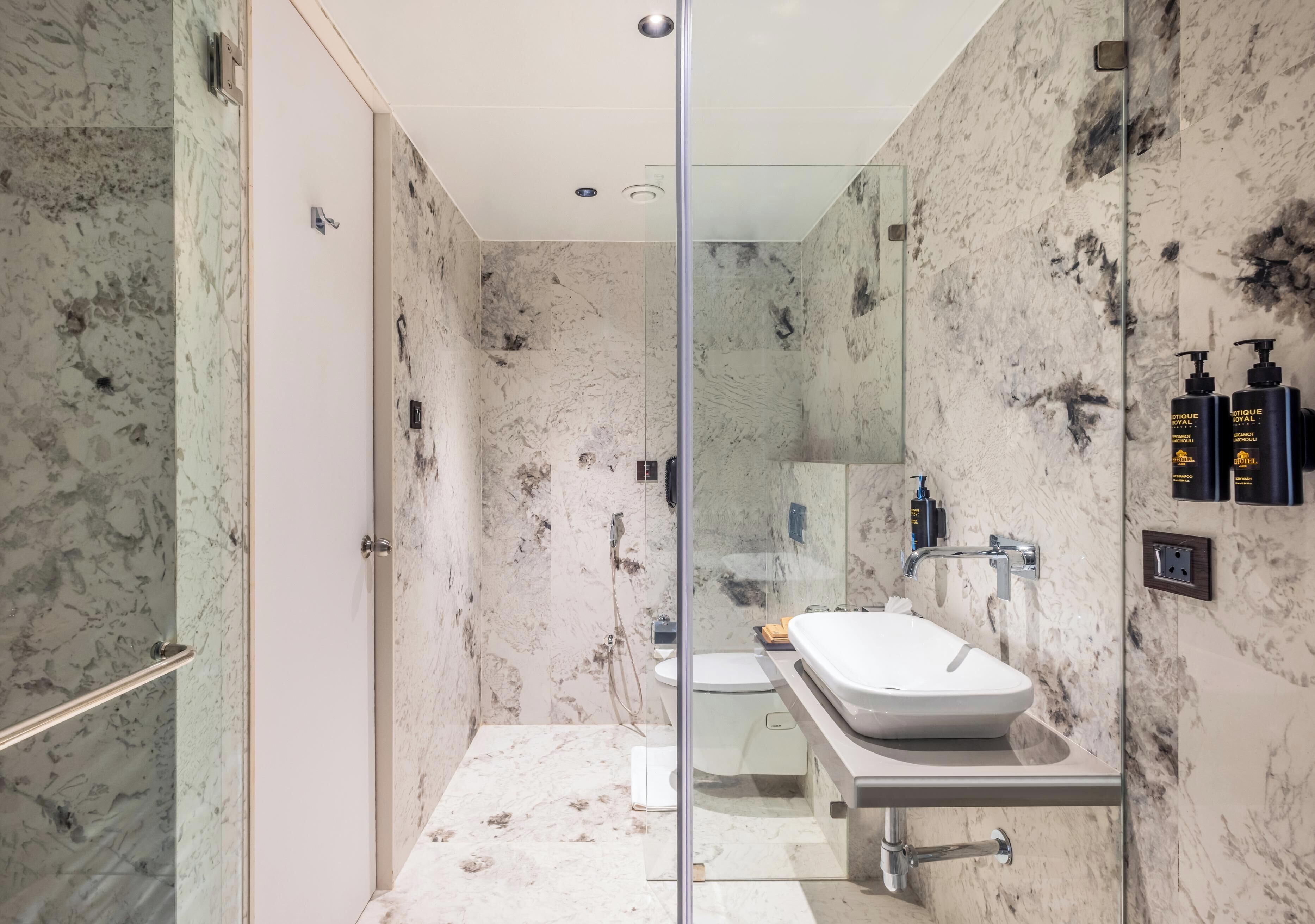 A modern bathroom with a glass shower enclosure, a white sink, and marble walls.