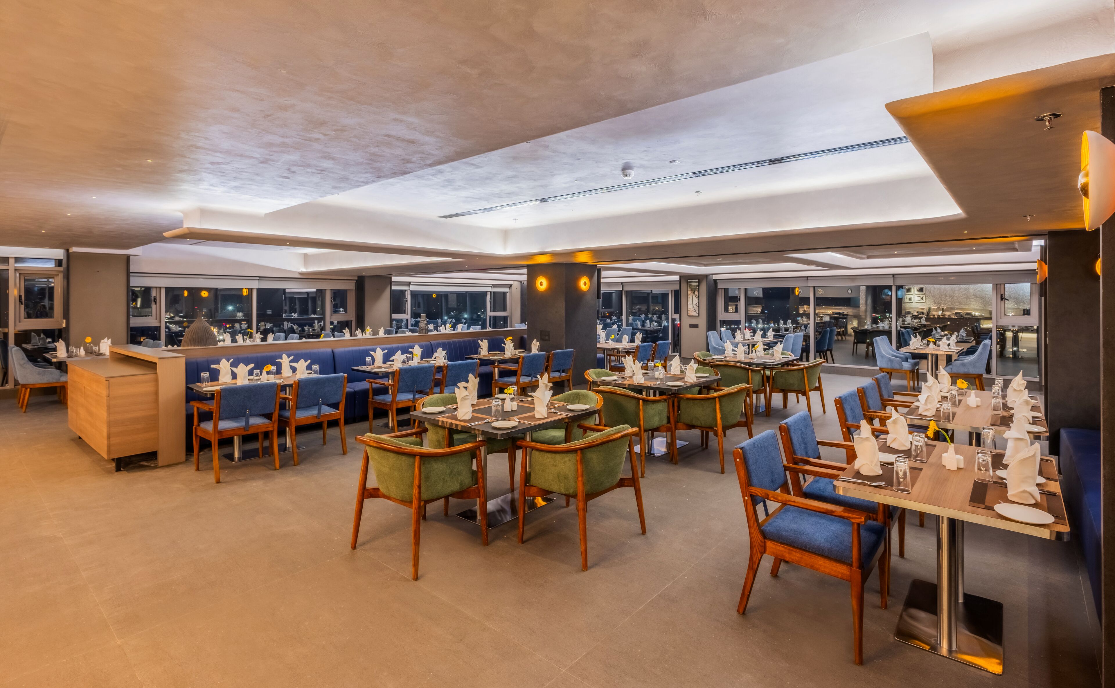 A modern restaurant with high tables and booths, large windows offering city views, and a clean, contemporary interior design.
