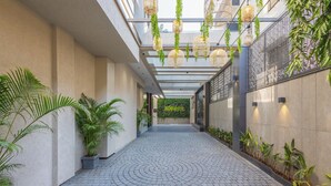 A corridor with a tiled floor, potted plants, hanging planters with greenery, and a patterned wall. - Effotel By Sayaji Sangli (Miraj)