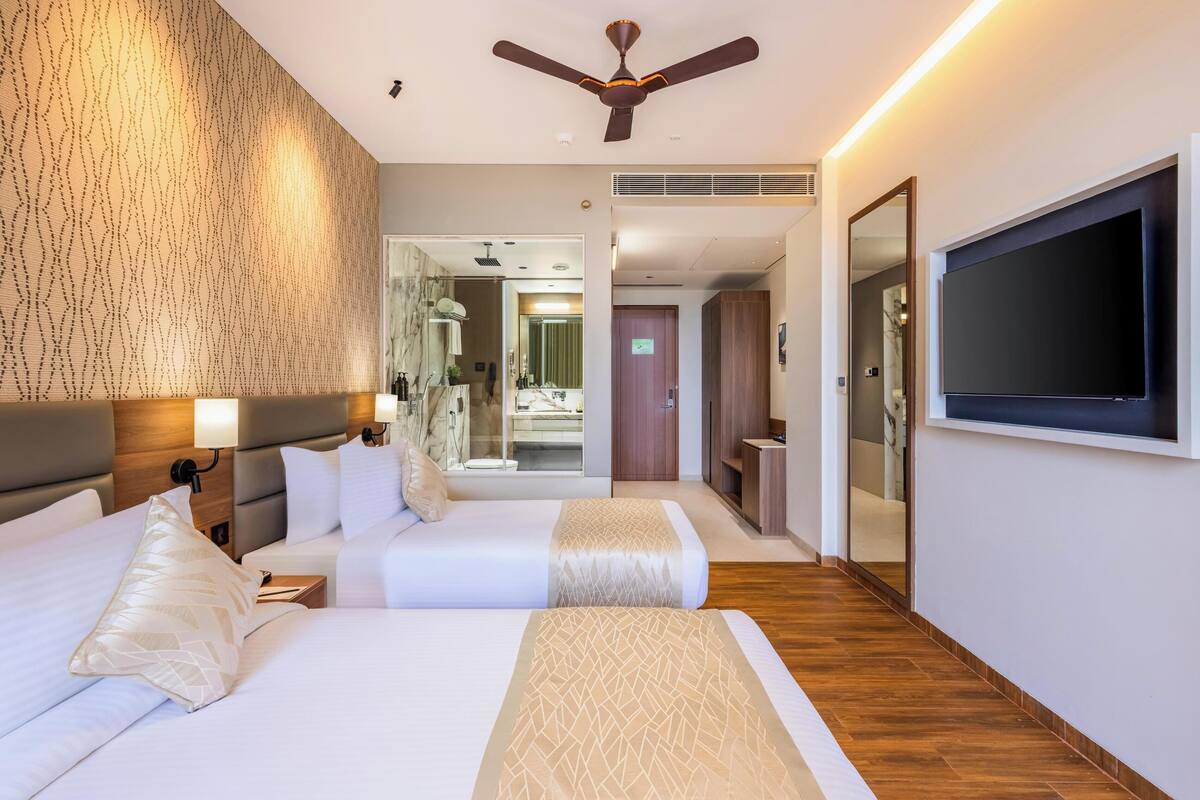 A hotel room with two beds, a ceiling fan, a TV, and a bathroom visible through an open door.