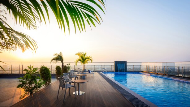 A rooftop pool with a wooden deck, lounge chairs, and palm trees. - Effotel By Sayaji Sangli (Miraj)