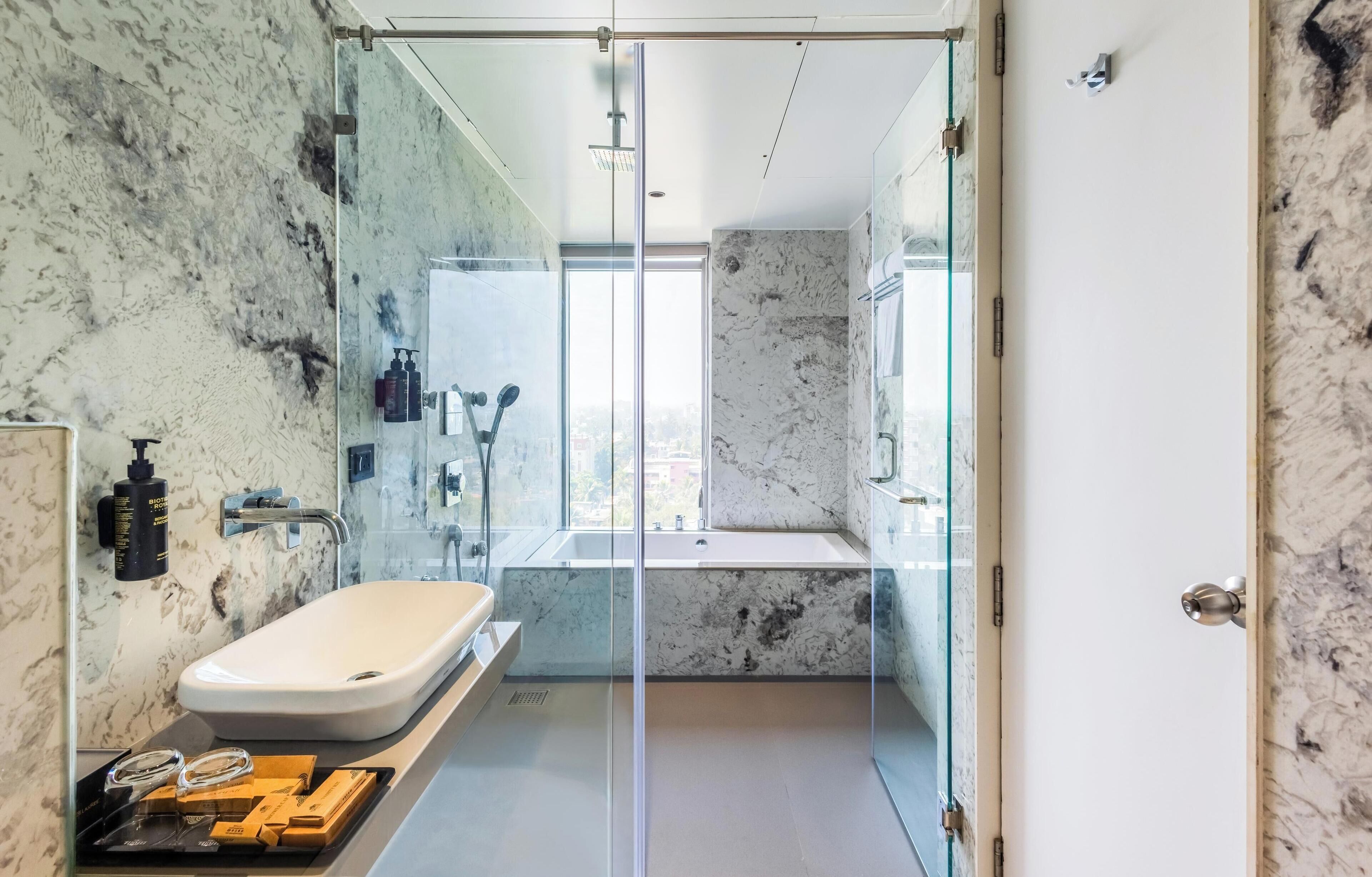 A modern bathroom with a glass-enclosed shower, a white sink, and marble walls.