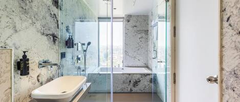 A modern bathroom with a glass-enclosed shower, a white sink, and marble walls.