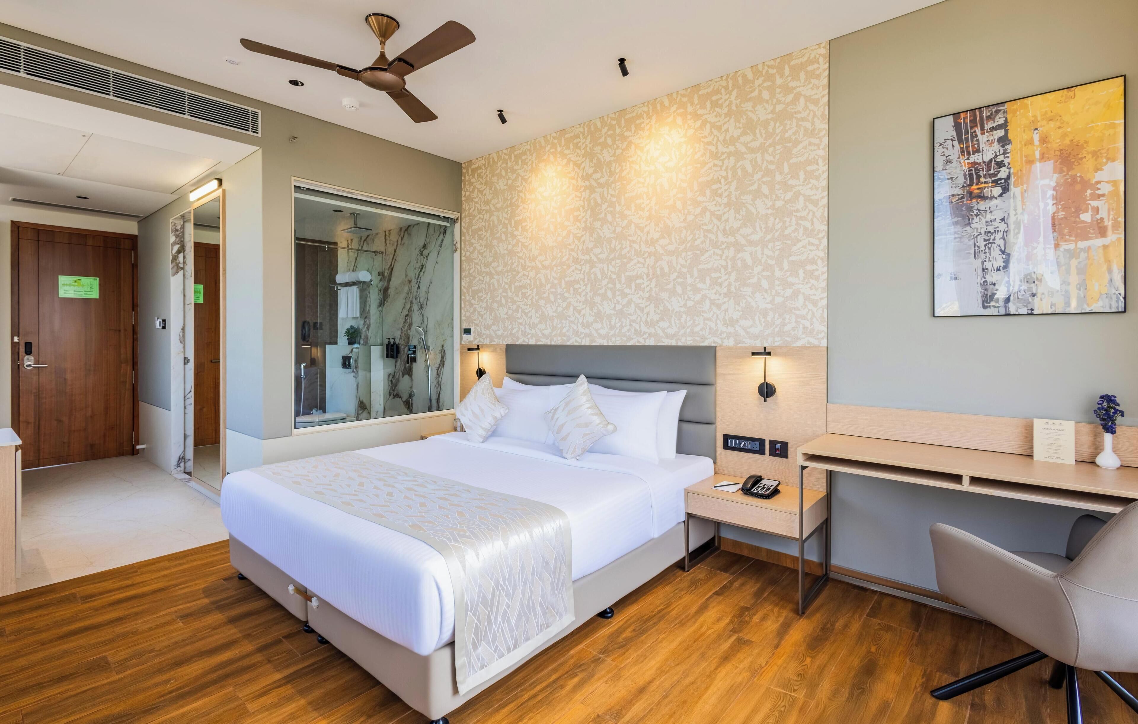 A modern hotel room with a large bed, a desk, and a ceiling fan.