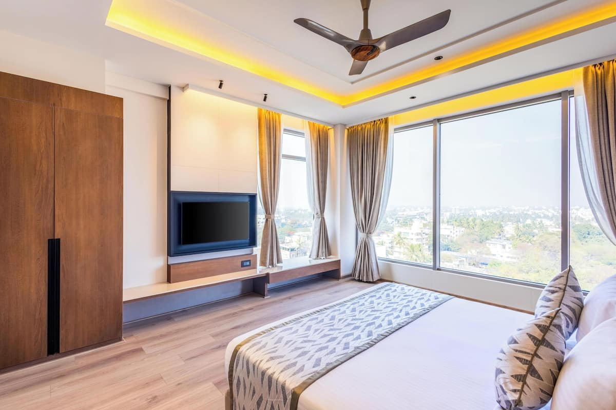 A modern hotel room with a large bed, a flat-screen TV, wooden wardrobe, and a city view.