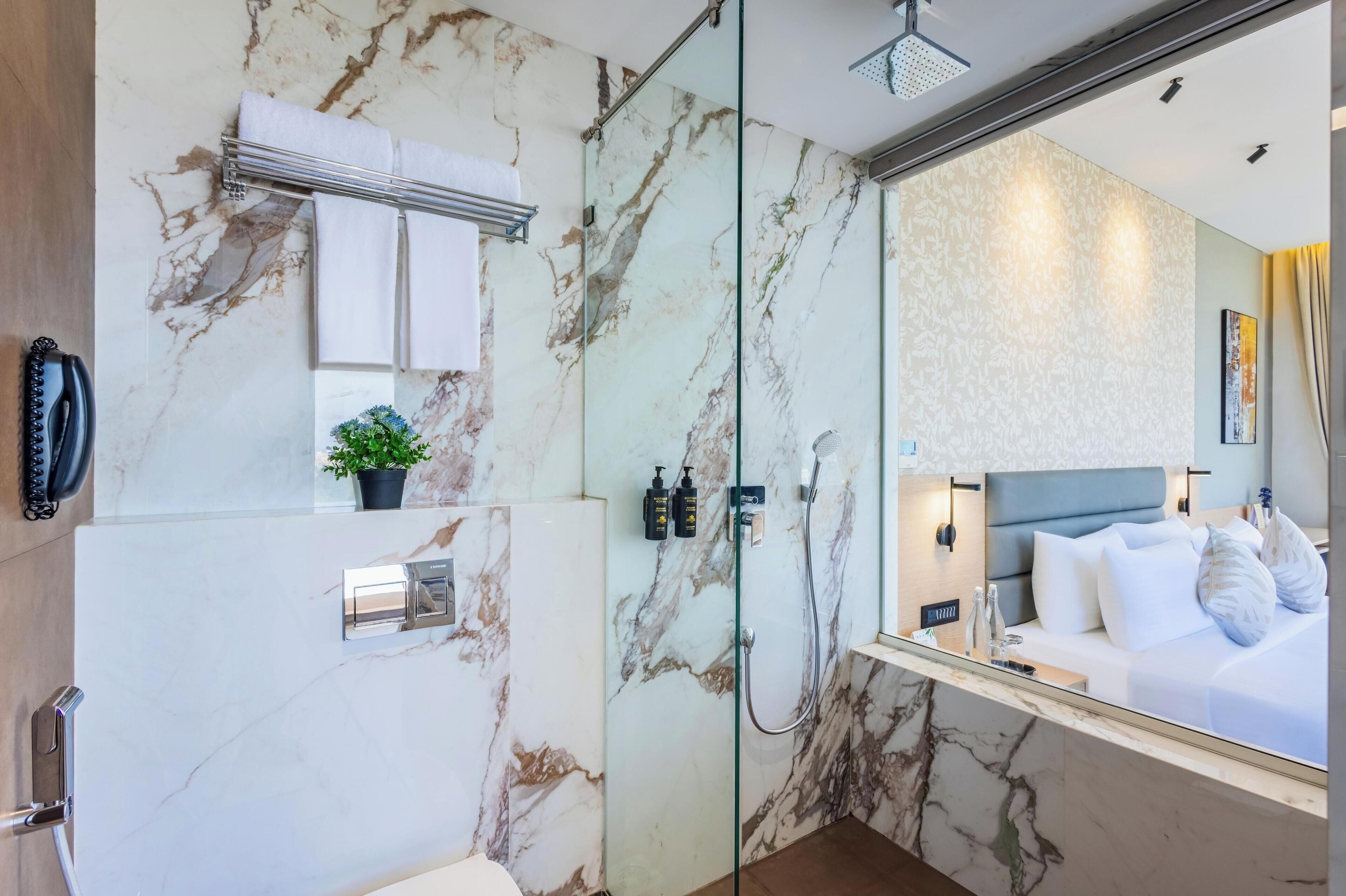 A modern bathroom with a marble wall, a glass shower enclosure, a mounted phone, and a small potted plant.