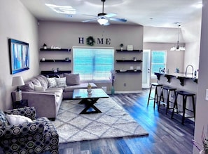 A living room with a sofa, coffee table, and a wall-mounted shelf with the word 'HOME'.