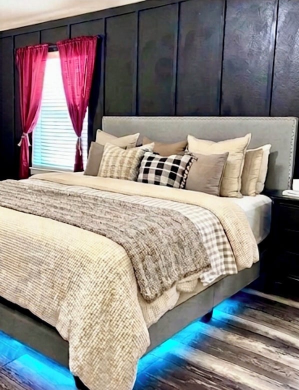 A bed with a grey headboard, multiple pillows, and a checkered blanket.