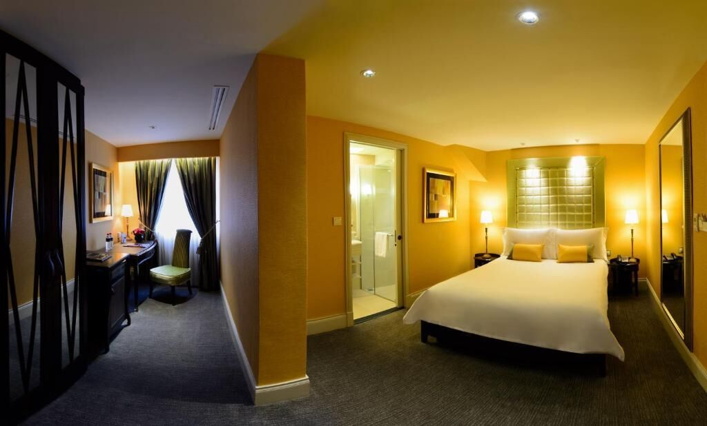 Una camera d'albergo con un letto grande, comodini, una scrivania con una sedia, uno specchio e un'apertura che dà su un bagno.